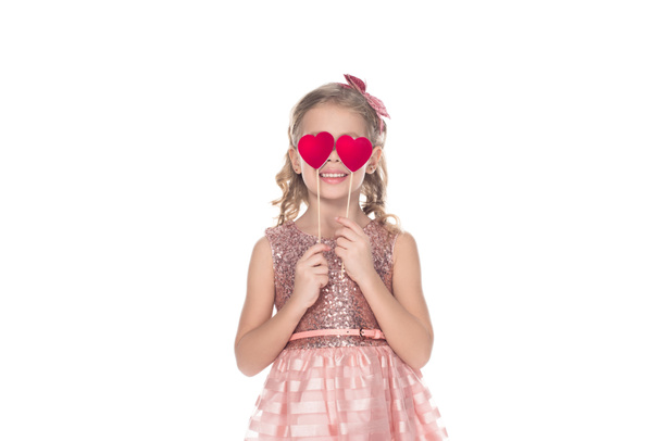 mooie lachende kindje in roze jurk rode harten houden op stokjes geïsoleerd op wit - Foto, afbeelding