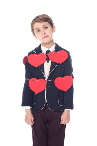upset little boy in suit staying tied with rope and red hearts, looking at camera isolated on white   - Foto, immagini