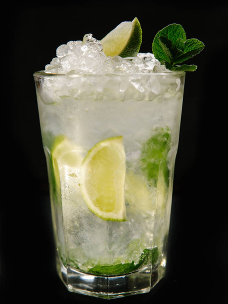 Mojito cocktail with ice, pepper mint and lime pieces on black background - 写真・画像