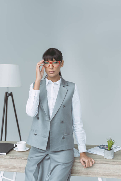 businesswoman touching glasses and looking at camera isolated on gray - Foto, afbeelding