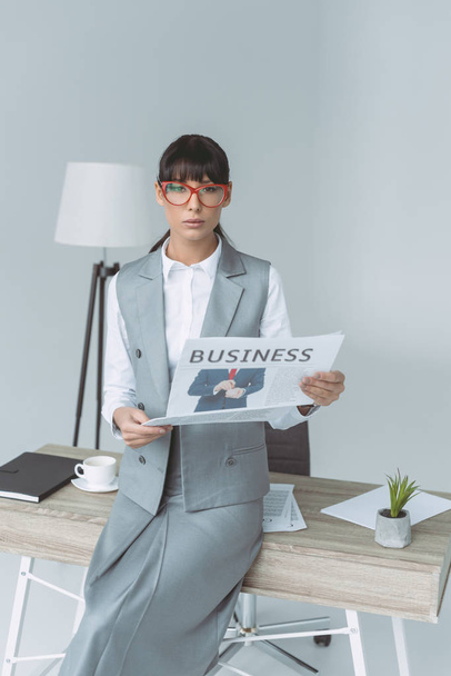 businesswoman holding newspaper and looking at camera isolated on gray - Foto, immagini