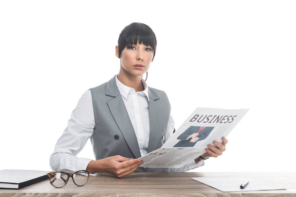 businesswoman sitting at table and holding business newspaper isolated on white - Fotografie, Obrázek