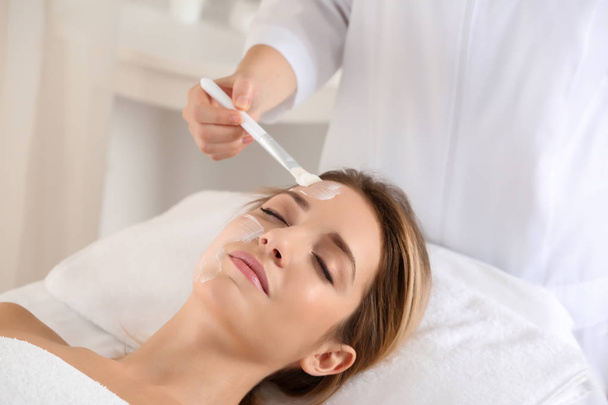 Beautician applying cream on young woman's face in spa salon - Foto, immagini