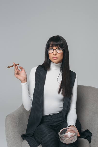 beautiful brunette businesswoman with ashtray and cigar isolated on gray - Photo, Image