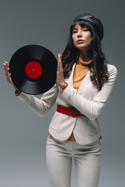 attraktive brünette Frau im weißen Anzug hält Vinyl isoliert auf grau - Foto, Bild