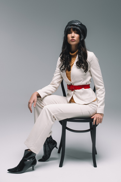 beautiful brunette woman in white suit sitting on chair on gray - Foto, afbeelding