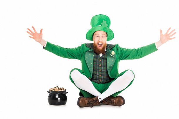excited leprechaun gesturing and sitting at pot of gold, isolated on white  - Photo, Image