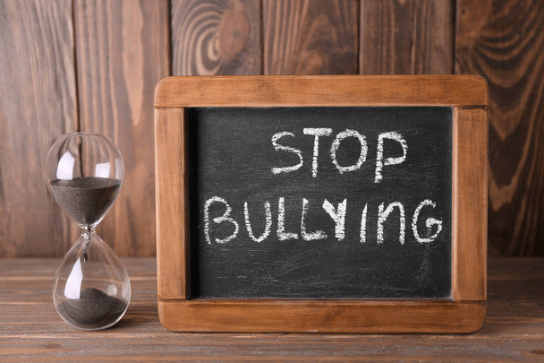 Chalkboard with text STOP BULLYING and hourglass on wooden background - Foto, afbeelding