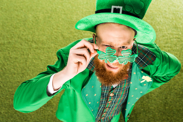 high angle view of bearded man in green costume wearing clover shaped eyeglasses and looking at camera, st patricks day concept - Φωτογραφία, εικόνα