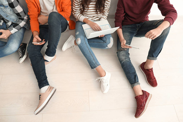 Group of teenagers with modern devices sitting on floor - 写真・画像