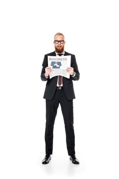 bearded young businessman in eyeglasses holding newspaper and looking at camera isolated on white - Foto, Imagen