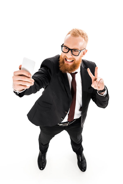 high angle view of smiling bearded businessman taking selfie with smartphone isolated on white - Foto, Imagem