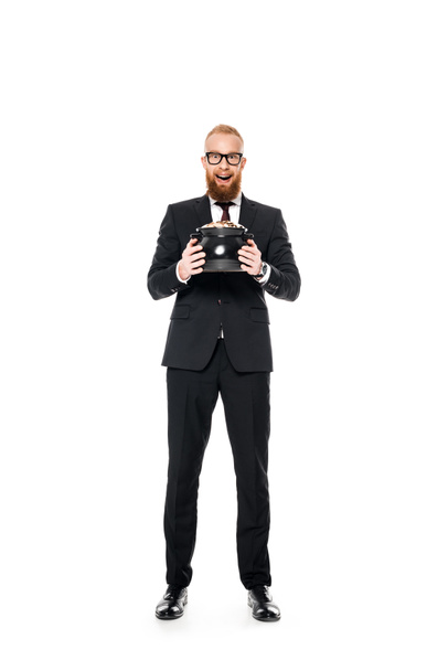 excited bearded businessman in eyeglasses holding pot with coins and looking at camera isolated on white  - Foto, Imagen