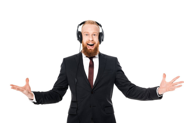 excited bearded young businessman listening music in headphones and looking at camera isolated on white - Photo, Image