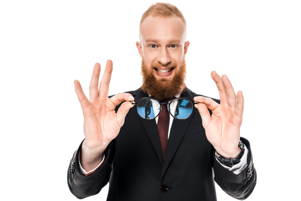 bearded young businessman holding eyeglasses and smiling at camera isolated on white - Фото, зображення