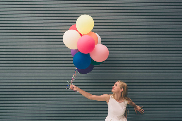 Счастливая молодая женщина с красочными воздушными шарами на улице рядом с серой - летняя концепция на открытом воздухе
 - Фото, изображение