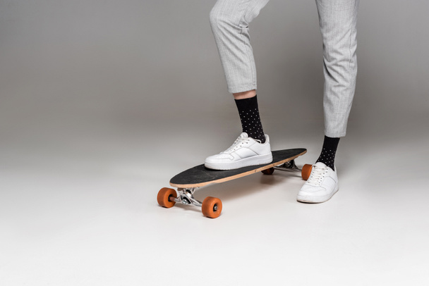 low section of stylish man standing on skateboard on grey - Φωτογραφία, εικόνα