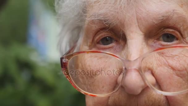 Vanha nainen silmälaseissa kääntää päätään ja katsoo kameraan. Mummilla on silmälasit ulkona. Isoäidin muotokuva ulkona. Sulje hitausliike
 - Materiaali, video