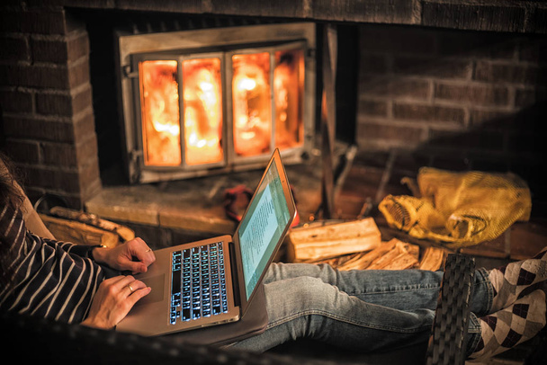 Женщина, работающая с ноутбуком в тепле камина
. - Фото, изображение