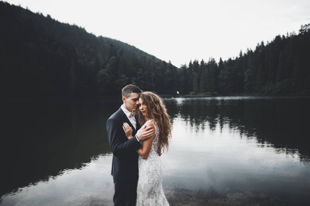 Young newly wed couple, bride and groom kissing, hugging on perfect view of mountains, blue sky - Foto, afbeelding