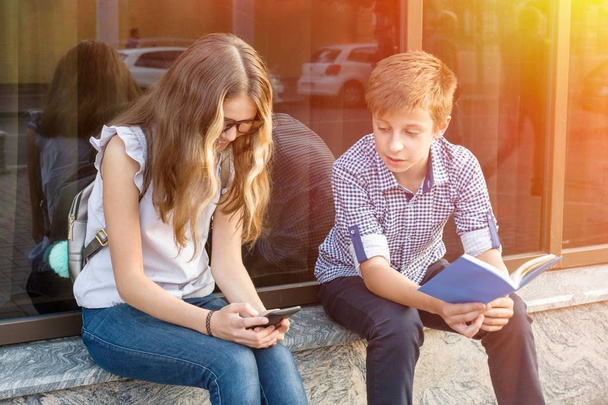 Children teenagers, reading book and using smartphone. - Zdjęcie, obraz
