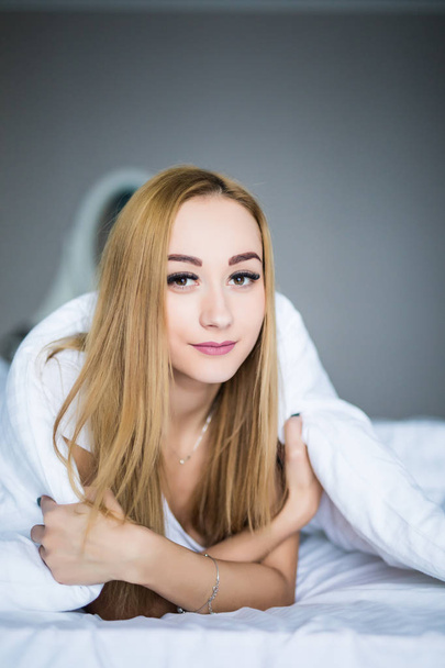 Jonge vrouw schoonheid liggen onder een dekbed in een slaapkamer - Foto, afbeelding
