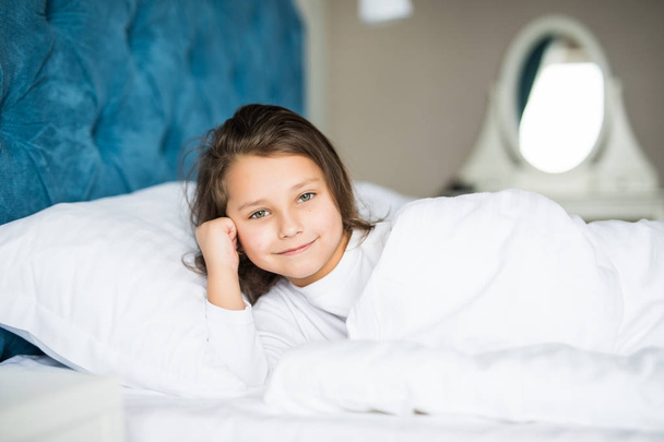 Close-up portret piękne małe dziecko leżąc na łóżku z ręką pod poduszkę, patrząc na kamery - Zdjęcie, obraz