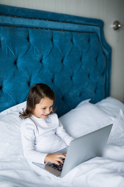 Menina deitada na cama e brincando com um laptop em seu quarto
. - Foto, Imagem
