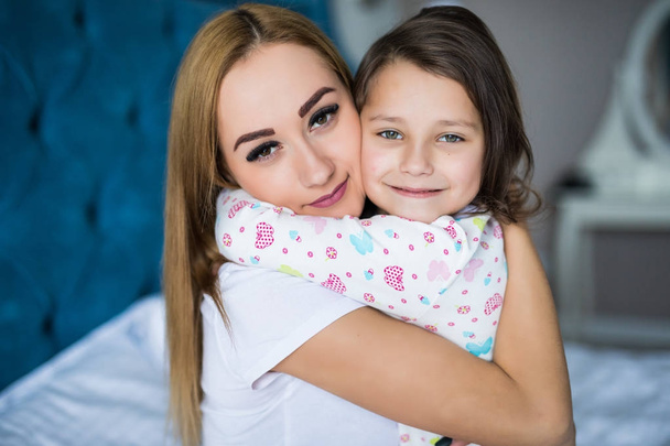 Mother and little daughter enjoy in bed at home and looking at the camera - Photo, Image