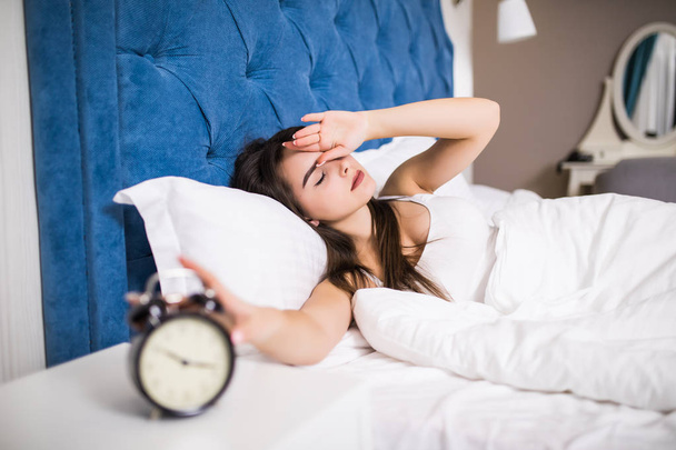 Sleepy young beauty woman stretching hand to ringing alarm to turn it off. Early wake up, not getting enough sleep, getting work concept. - Photo, Image