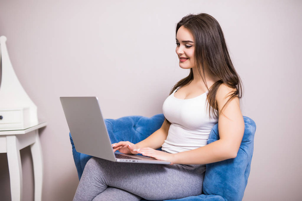 Młoda kobieta siedzi na krześle z laptopa w domu - Zdjęcie, obraz