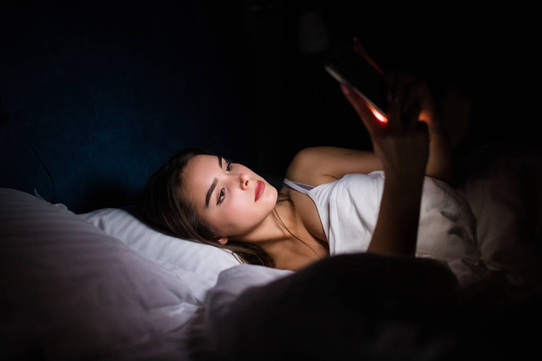 Una mujer usando teléfono inteligente en la cama por la noche en casa
 - Foto, imagen
