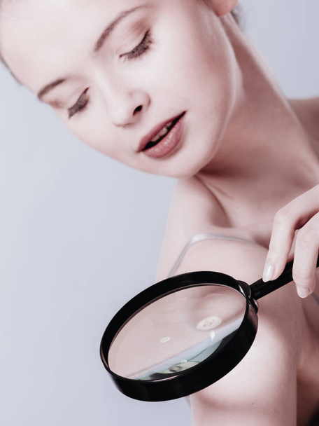 Woman using magnifying glass to examine her moles skin - Foto, immagini