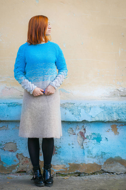 Una bella giovane donna con i capelli rossi in un maglione blu fatto di lana naturale e gonna beige di lana sorridente e in posa su una strada della città
 - Foto, immagini