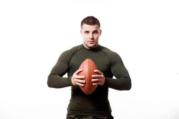 Un joven luchador de cabello oscuro en un rashgard deportivo verde sonríe y sostiene una pelota de rugby en las manos de un fondo blanco aislado
 - Foto, Imagen