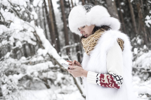 Νεαρή γυναίκα με το κινητό στο χειμωνιάτικο τοπίο. Πληκτρολογώντας ένα μήνυμα - Φωτογραφία, εικόνα