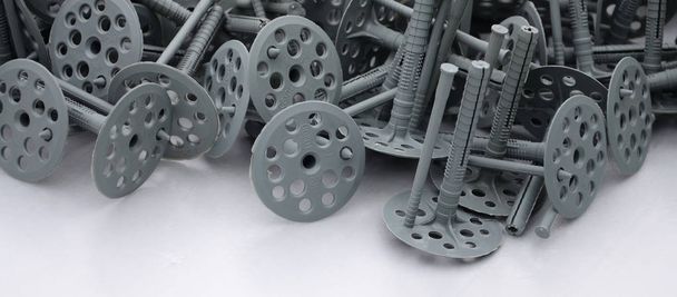 Background of many gray plastic dowels (fastening) for thermal insulation. A huge pile of plastic bolts with round holey hats lies on a gray foam polystyrene plate - Photo, Image