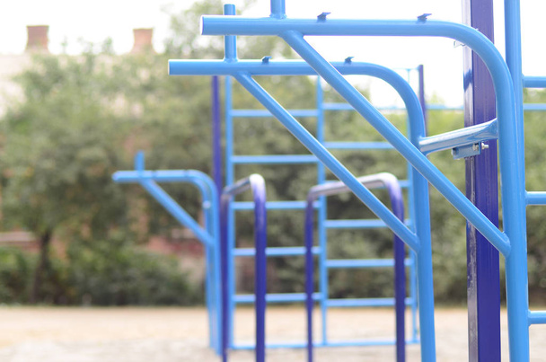 Sportbars in blau auf dem Hintergrund eines Straßensportplatzes für das Training in der Leichtathletik. Fitnessgeräte für den Außenbereich. Makroaufnahme mit selektivem Fokus und extrem unscharfem Hintergrund - Foto, Bild