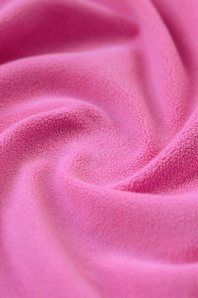 Одеяло из пушистой розовой шерстяной ткани. Фон светло-розовый мягкий плюшевый материал с большим количеством рельефных складок
 - Фото, изображение