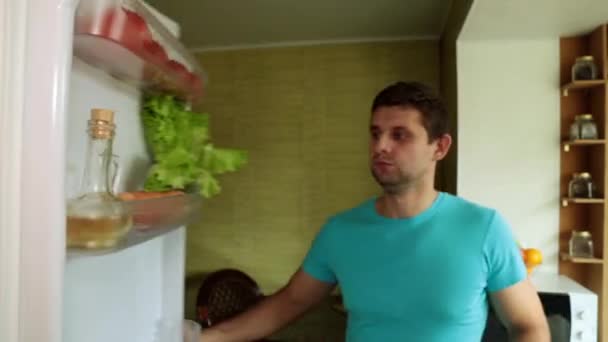 A man takes meat from the refrigerator. A man in the kitchen opens the fridge. - Video