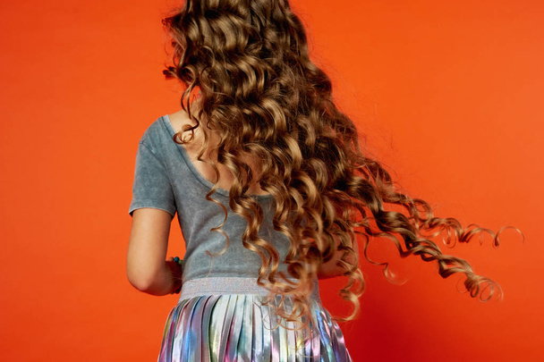 Girl on orange background in the Studio. Very long curly hair like in a fairy tale.Rapunzel. developing in the movement - Foto, Bild