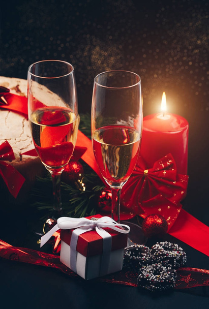 Weihnachten oder Neujahr. Champagner in Gläsern mit Kerzen, Panettone und Geschenk mit roter Satinschleife. Kopierraum. Urlaubskonzept - Foto, Bild