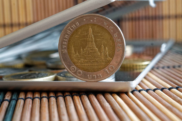 Montón de monedas con una denominación de moneda frontal de 10 baht en espejo reflejan billetera se encuentra en fondo de mesa de bambú de madera
 - Foto, imagen