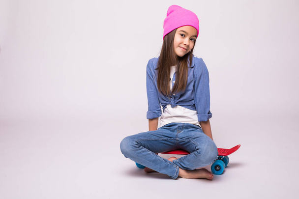 Happy little girl in rose hat skateboarder sitting on longboard, isolated on white background - Zdjęcie, obraz