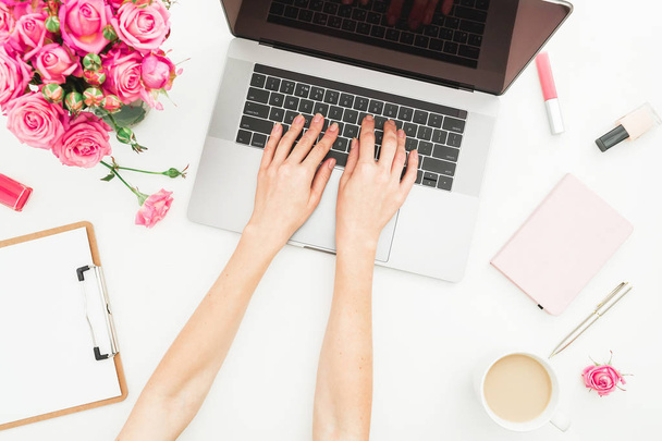 Home office desk. Woman workspace with female hands, laptop, pink roses bouquet, accessories, diary on white. Top view. Flat lay. Girl working on laptop. - Foto, Imagen