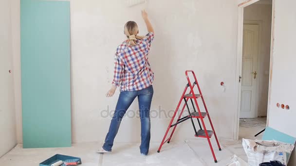 Slow motion beelden van gelukkige jonge vrouw muur schilderen en dansen op Nieuw appartement - Video