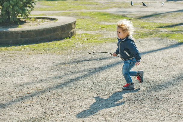 Happy toddler in blue jacket and jeans run with stick - Zdjęcie, obraz