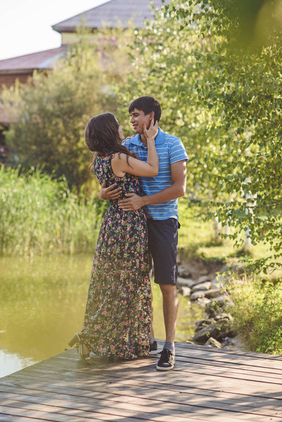 Ευτυχισμένο ρομαντικό ζευγάρι στο χωριό, βόλτα στην ξύλινη γέφυρα κοντά στη λίμνη. Νεαρή όμορφη γυναίκα και άντρας αγκαλιάζονται.. - Φωτογραφία, εικόνα