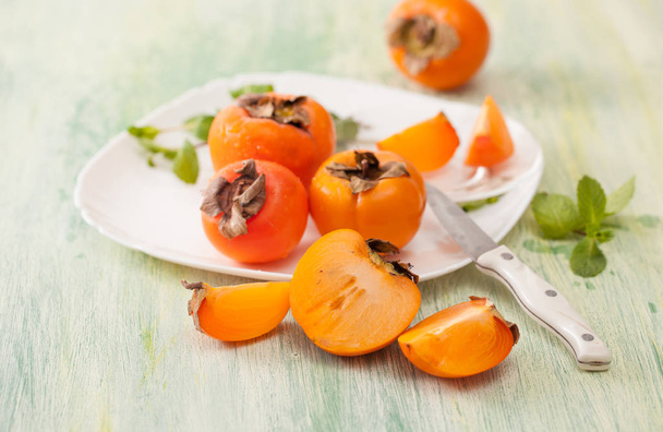 Fresh ripe persimmons in a dish on the kitchen table - Фото, изображение