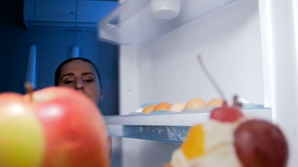 4k footage of hungry smiling woman looking for something to eat and taking sweet cake from refrigerator at night - Filmagem, Vídeo